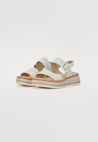 White woven sandals with a textured upper and a cushioned footbed. Features a wide strap and adjustable buckle. Platform sole with a wood look.