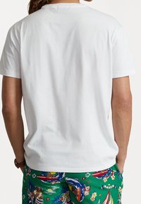 Wit katoenen T-shirt met een ronde hals, korte mouwen en een rechte zoom aan de achterkant, gecombineerd met kleurrijke korte broek met patroon.