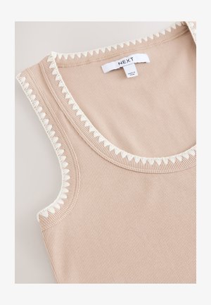 Bēša ribota tanktop ar baltu stūrveida apmali pie kakla un roku atverēm. Iekšpusē zīmogs ar uzrakstu "NEXT". Mīksta tekstūra.