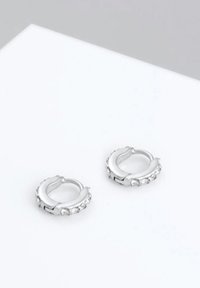 Srebrni obroči za ušesa okrašeni s prozornimi kamni. Gladka tekstura z poliranim zaključkom in zaobljena, rahlo debela zasnova.