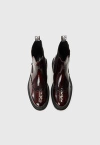 Stivali Chelsea in pelle lucida bordeaux con dettagli brogue, pannelli laterali elasticizzati e linguetta, dotati di una robusta suola in gomma nera.