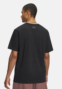 Sort bomulds T-shirt med rund hals, korte ærmer og et diskret logo på ryggen. Glat tekstur og afslappet pasform.