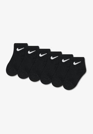 Six paires de chaussettes noires montant à la cheville avec des logos Nike swoosh blancs alignées en rangée sur un fond blanc.