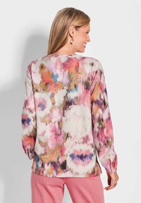 Bluse mit Blumenmuster in sanften Tönen von Pink, Lila und Beige, mit langen Ärmeln und rundem Ausschnitt. Weicher, fließender Stoff.