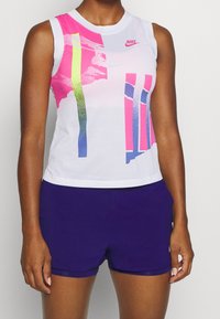 Top senza maniche Nike realizzato in tessuto a rete bianco con grafiche nei colori rosa, verde e blu; abbinato a pantaloni corti viola.