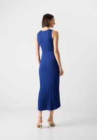Robe maxi sans manches, en bleu, avec des côtes, dotée d'un corsage ajusté et d'une jupe évasée, présentant un ourlet au genou, associée à des sandales à talons beiges.