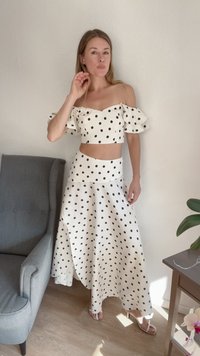 Top cropped branco com bolinhas pretas e babados à clara, combinado com uma saia de cintura alta a condizer, ambos com um design fluido.