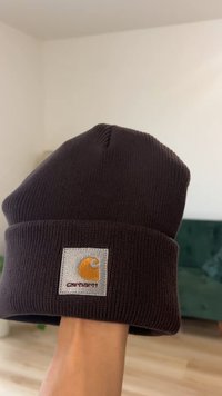Brązowa dziergana czapka typu beanie z mankietem, z prostokątną szarą naszywką z pomarańczowym stylizowanym logo na przodzie.