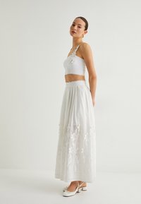 Witte twee-delige outfit bestaande uit een cropped top met een bloemenaccent en een rok met geborduurde bloemen en een gestructureerde zoom. Slingback schoenen inbegrepen.