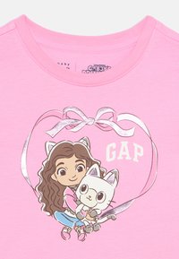 Κορίτσι κινουμένων σχεδίων με αυτιά γάτας που αγκαλιάζει μια λευκή γάτα μέσα σε κορδέλα σε σχήμα καρδιάς με την επιγραφή «GAP» σε ροζ ύφασμα.