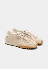 Baskets en daim beige avec une tige légère et texturée, un bout rond, des lacets plats et une semelle extérieure en caoutchouc naturel avec de petits points pour la traction.