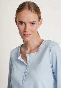 Lichtblauw henley-shirt van zachte stof, met een ronde halslijn en vier knopen aan de voorkant. Lange mouwen met een zachte textuur.