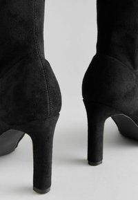 Schwarze Wildleder-Ankle Boots mit hohen Absätzen, glatter Textur, spitzen Zehen und einem schmal zulaufenden Absatz, mit einem subtilen Nahtdetail.