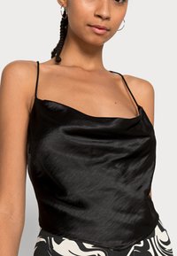 Camisola preta de seda com alças finas, apresentando um decote drapeado e uma textura suave e brilhante. Combinada com uma parte inferior estampada.