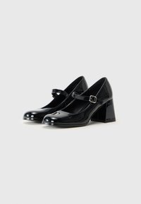 Black patent leather Mary Jane heels with a square toe, ankle strap, and chunky block heel. Smooth texture and shiny finish.