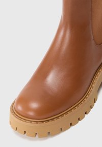 Bottine en cuir marron à finition lisse, bout arrondi, panneaux latéraux élastiques et semelle en caoutchouc épaisse avec rainures profondes.