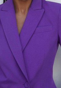 Blazer violet avec un col cranté, une fermeture à un bouton et une petite poche poitrine. Tissu lisse avec une coupe ajustée.