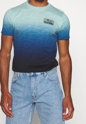 Kortärmelig T-shirt met een verloop van lichtblauw naar donkerblauw, voorzien van een klein zwart "Hollister California" logo aan de linkerbovenkant.