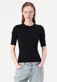 Sort kortærmet t-shirt lavet af ribbet stof, med rund halsudskæring og en tætsiddende silhuet. Kombineret med lysvaskede denimjeans.