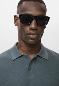 Black sunglasses and gray polo shirt with a textured knit pattern and two buttons at the collar, model's face partially visible.