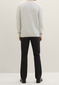 Maglione grigio chiaro, strutturato, con polsini e orlo a costine, abbinato a pantaloni scuri a gamba dritta e scarpe nere. Sfondo neutro.