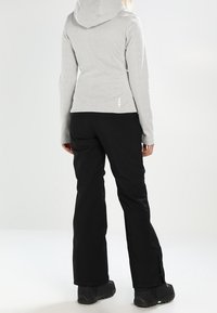 Sudadera con capucha texturizada y gris, de diseño ajustado, combinada con pantalones negros de corte holgado. Calzado negro con un acento verde.