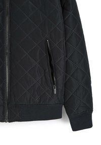 Czarna pikowana kurtka z rombowym wzorem, dwoma bocznymi kieszeniami na zamek, ściśniętymi mankietami i dołem wykonana z gładkiego, lekkiego materiału.