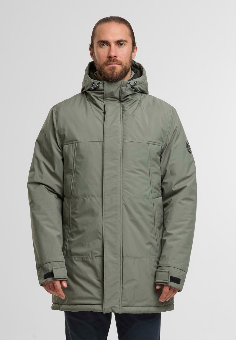 Giacca imbottita verde con colletto alto, cappuccio regolabile e due tasche frontali. Presenta dettagli in velcro nero e una patch con il logo sulla manica.