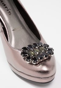 Chaussure à talon haut rose métallisé avec un carré de pierres précieuses noires et vertes facettées sur l’avant.