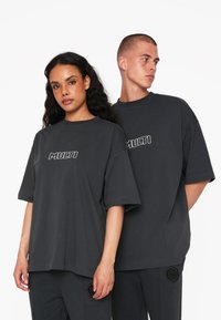 Mørkegrå oversized t-shirts med korte ærmer har et hvidt "MULTI" logo på fronten. Synlige teksturerede detaljer på bukserne.