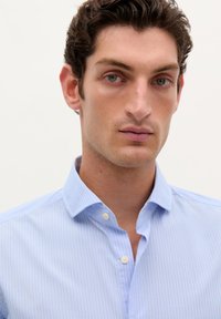 Lichtblauwe button-up shirt met fijne witte strepen, puntige kraag en een nette textuur. De voorkant heeft twee knopen bij de kraag.