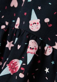 Tessuto blu navy scuro con fantasie giocose di coni gelato, orsetti sorridenti, cuori e stelle in colori rosa e pastello con dettagli arricciati.