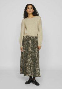 Beige garšām piedurkņu džemperis saskaņots ar zaļganu un brūnu leopardu rakstu maxi svārku. Svārki ir plūstoša dizaina ar jostas vietu. Valkā melnus mokasīnus.