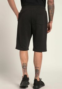 Shorts en coton noir avec une taille élastique, une poche arrière unique et une coupe au genou. Tissu texturé avec une finition lisse.
