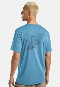 Blauwe katoenen t-shirt met een grafisch ontwerp op de achterkant met topografische elementen, coördinaten en lijntekeningen. Korte mouwen en een relaxte pasvorm.