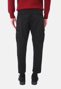 Pantaloni cargo neri con tasche laterali, taglio dritto e polsini regolabili. Il tessuto è liscio con una finitura opaca. Indossati con scarpe nere.
