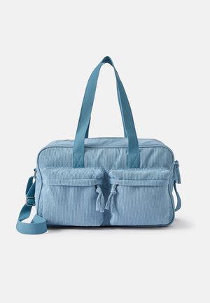 Blue corduroy bag with dual front pockets, soft texture, two handles, and an adjustable shoulder strap. Two zipper pulls with tassels.