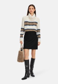 Chunky Strickpullover mit Creme-, Braun- und blauen Streifen, schwarzer Minirock, kniehohe schwarze Lederstiefel und beigefarbene Kunstfelltasche.
