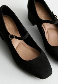 Tacchi Mary Jane in suede nero con punta quadrata, piccolo tacco a blocco e cinturino rotondo con fibbia dorata. Fodera interna color beige chiaro.