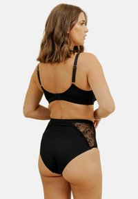 Un soutien-gorge noir et un slip taille haute présentent des détails en dentelle sur les côtés, des bretelles réglables, un tissu lisse et une coupe ajustée.