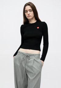 Top cropped preto de mangas compridas com textura canelada e pequeno logótipo de coração vermelho. Combinado com calças cinzentas de cintura alta, com cordão e pregas.