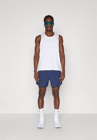 Biała bezrękawnikowa koszulka z małym logo, granatowe szorty, białe trampki i duże niebieskie okulary przeciwsłoneczne. Płaska, gładka faktura.