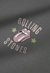 Grå T-shirt med texten "ROLLING STONES" och en rosa tunggrafik, dekorerad med rhinstenar och gröna stjärnaccenter.