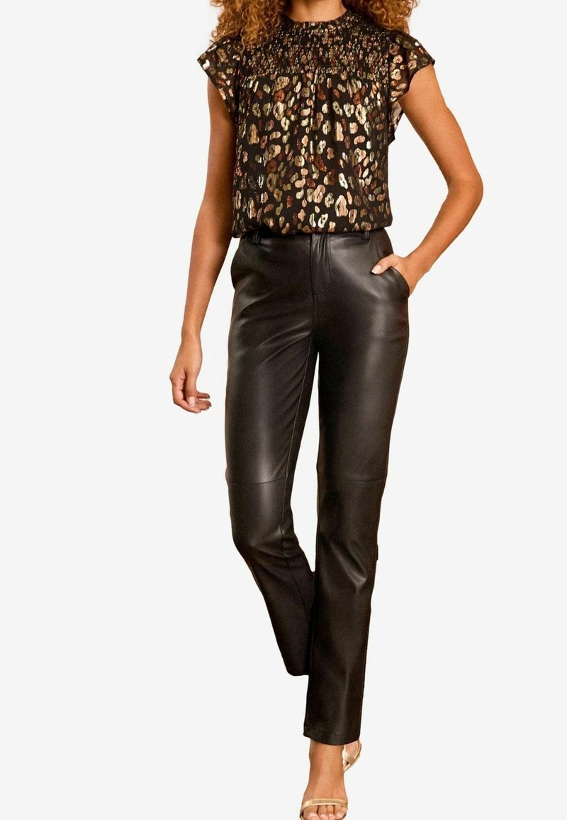 Black leather pants paired with a sheer top featuring a multicolored animal print, short sleeves, and a smocked neckline.