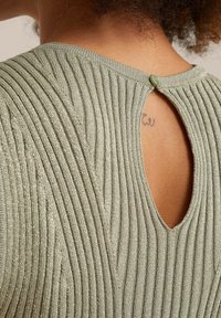 Texturerad stickad topp i ljusgrön med vertikal ribbning, ett nyckelhål baktill och en liten rund knapp vid halsen.