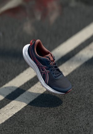 Blue and orange athletic shoe with a mesh upper, textured sole, and contrasting stripes, suspended above a road surface.