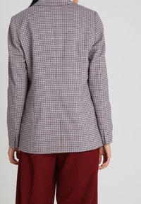 Strukturovaný blazer s mřížkovým vzorem v odstínech šedé, fialové a červené, s klopovým límcem a přiléhavým střihem, vyrobený z hladkého materiálu.