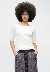 Wit, geribbeld kortärmelig topje gecombineerd met een knielange rok met blauwe knopen en een gestructureerde, meerkleurige stof.