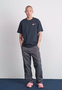 Black Nike t-shirt with logo, gray cargo pants, and pink sneakers. Person stands with hands in pockets against a light background.