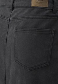 Jeans in denim nero con una sola tasca posteriore e un'etichetta in pelle marrone. Texture liscia con un design aderente e dettagli di cucitura scuri.